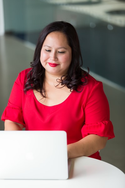 一个穿着红色上衣，用笔记本电脑微笑的女人
